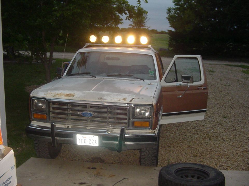 1980s Ford Bronco with a light bar on the roof and the driver's door open. License plate reads YCQ 22X