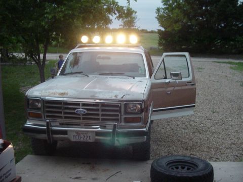 1982 Ford Bronco - This older model Ford Bronco is parked in a gravel driveway with its door open and auxiliary lights on the roof.
