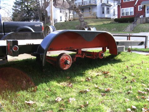 2005 Ford F-250 - A trailer with red fenders and dual axles is parked on grass next to a pickup truck.