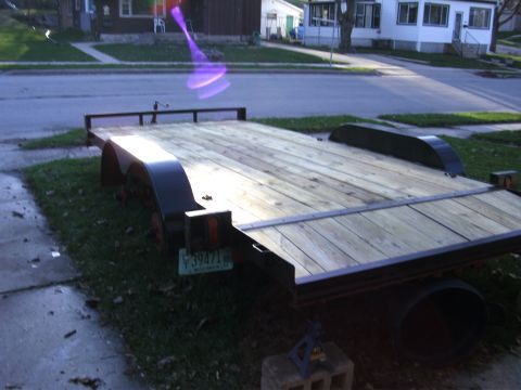 2005 Ford F-250 - A utility trailer with a wooden deck is parked on a residential street.