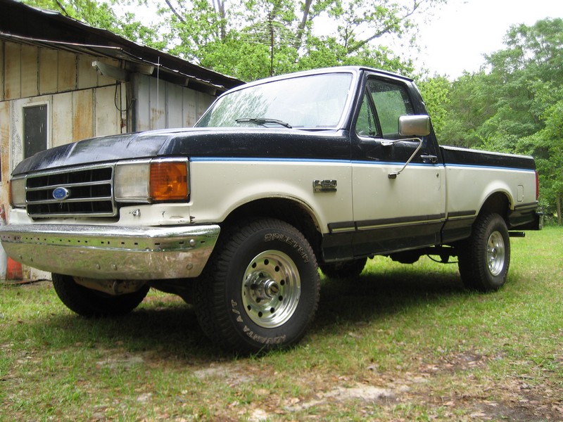 Two-tone Ford F-150 pickup truck parked on grass in front of a wooden building