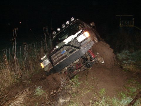 1996 Ford Bronco - A Ford Bronco is stuck in the mud on a dark, grassy slope, with its front end angled upwards.