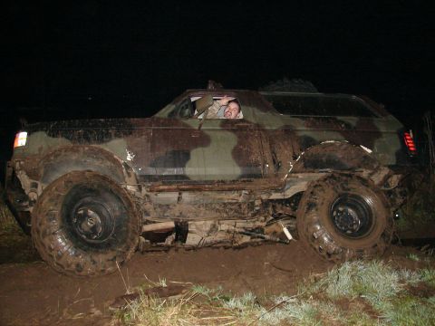 1996 Ford Bronco - A camouflaged SUV with oversized tires is stuck in the mud at night, with a person waving from the driver's side window.
