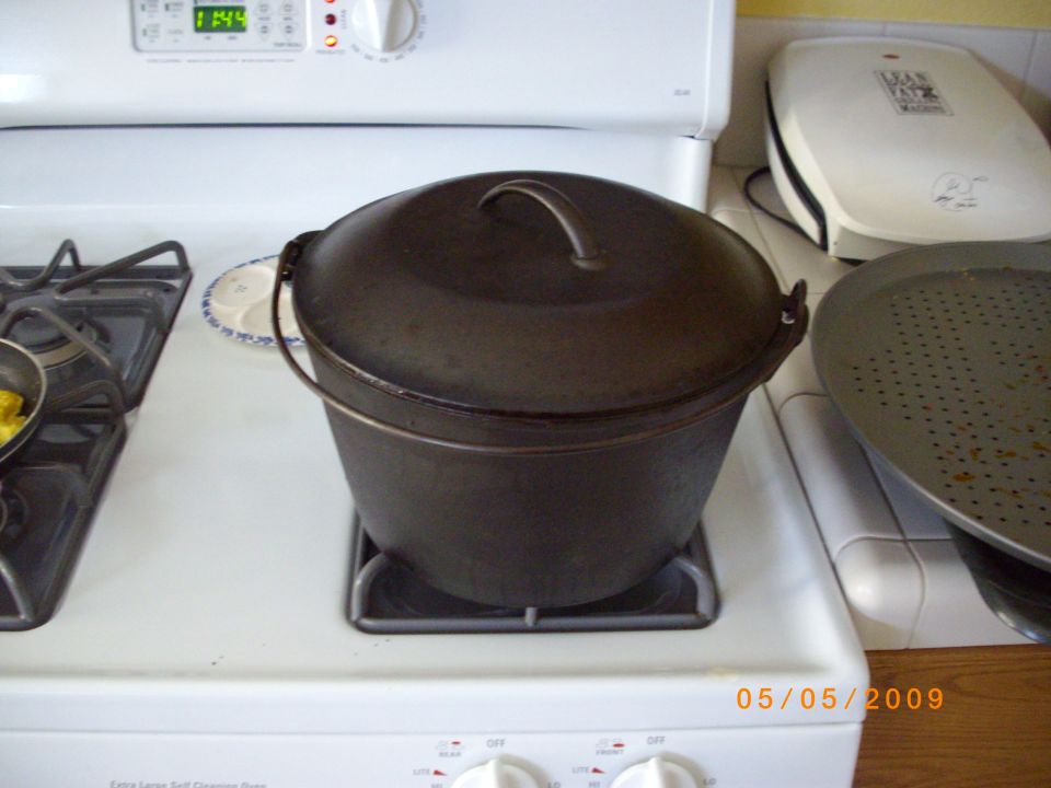 Cast iron dutch oven on a white gas stovetop next to a pizza pan and a waffle maker