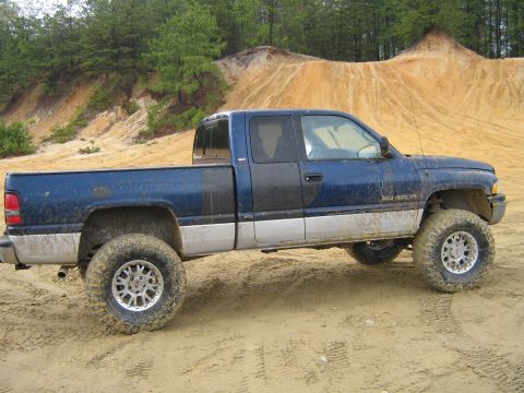 1990 Ford Bronco - A lifted blue pickup truck with aftermarket wheels navigates a sandy off-road course.