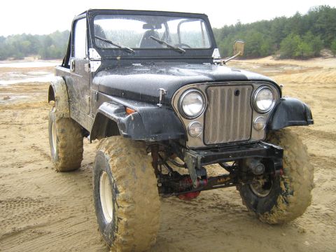 1990 Ford Bronco - This black Jeep CJ-7, equipped with large off-road tires, navigates a muddy terrain.