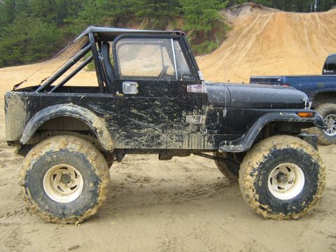1990 Ford Bronco - A muddy Jeep CJ-7 is shown off-road, with a blue pickup truck visible in the background.