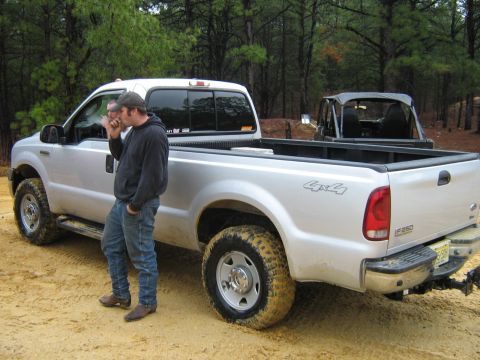 1990 Ford Bronco - A silver pickup truck is parked on a dirt road with a man standing beside it.