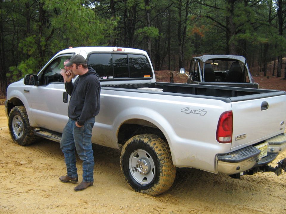 Silver pickup truck with 4x4 decal, rear view. Muddy tires, chrome bumper, F-250 badge