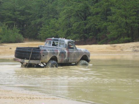 1990 Ford Bronco - This pickup truck is navigating through a muddy body of water with trees in the background.