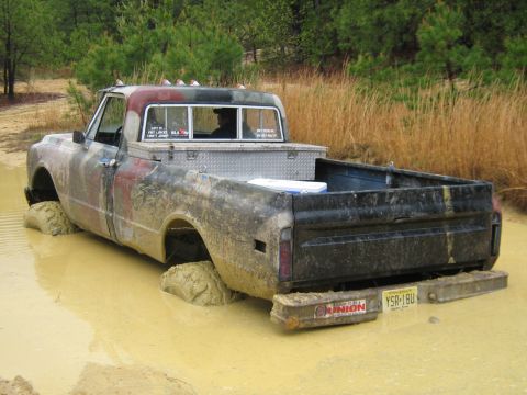 1990 Ford Bronco - Pickup truck stuck in mud, showing its rear end and license plate.
