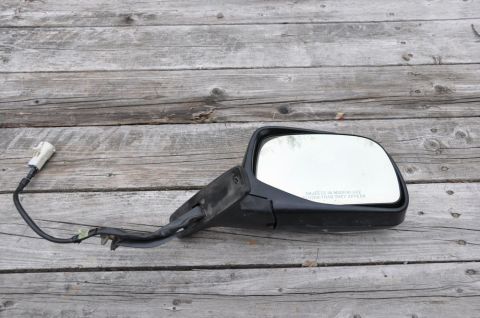 1996 Ford Bronco - A black side view mirror with a white electrical connector rests on a weathered wooden surface.