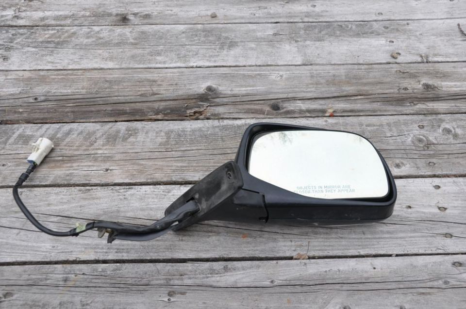 Side view mirror with wiring harness attached, lying on wooden planks
