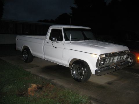 1995 Ford Bronco - A white 1975 Ford F-100 pickup truck is parked outside at dusk, showing its front grille and Cooper Cobra tires.