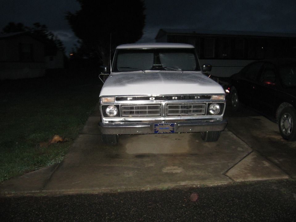 White Ford F-Series truck parked in driveway at dusk. Another car is parked to the right