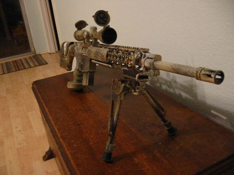 1996 Ford Bronco - Assault rifle with scope and bipod, covered in camouflage paint, rests on a wooden surface.