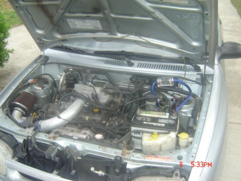 1995 Ford Aspire - The engine bay of a silver car is visible with the hood open, revealing the engine components and battery.