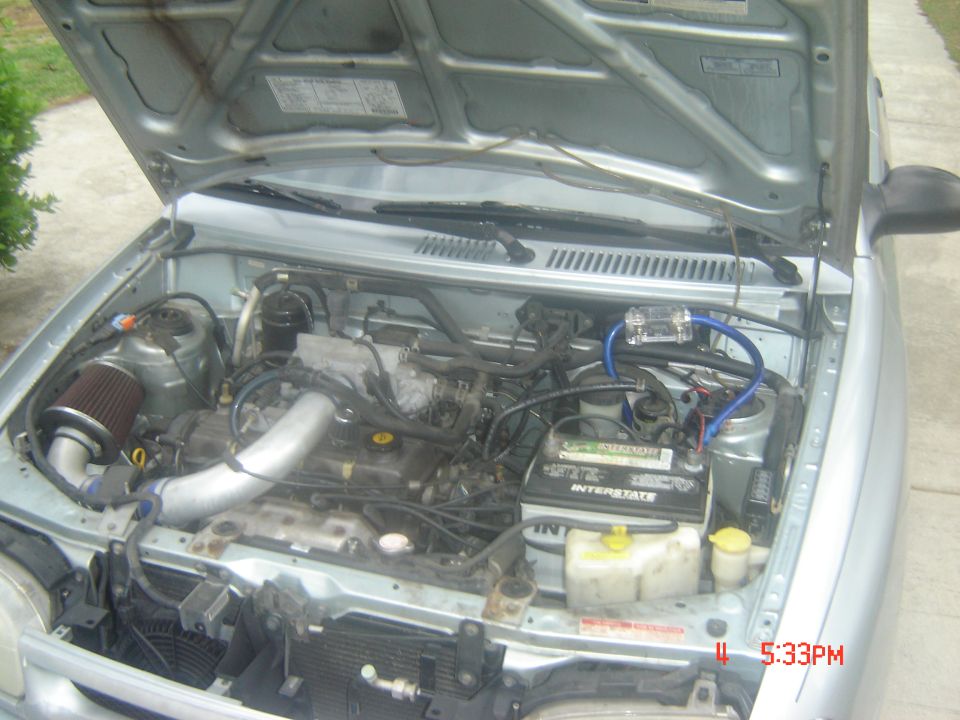 Silver car engine bay with hood open, showing engine, battery, and air intake