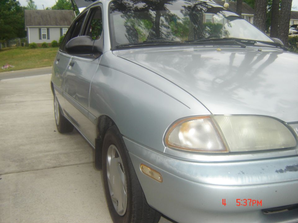 Silver sedan parked on a driveway. Trunk is open. Houses and trees in background