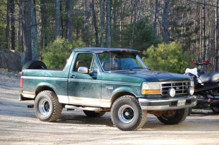 1993 Ford Bronco - This green Ford Bronco is parked on a dirt road with trees in the background.