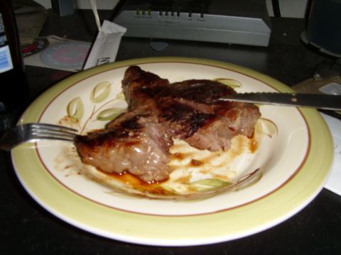 1978 Ford Bronco - A cooked steak sits on a decorative plate, ready to be eaten, with a bottle and electronic equipment visible in the background.