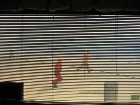 1996 Dodge 2500 - View through blinds shows two figures in racing attire on a paved surface, possibly a racetrack.