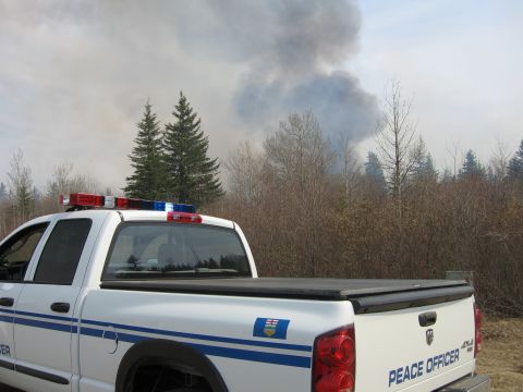 1996 Dodge 2500 - A white pickup truck marked "Peace Officer" is parked near a scene with a large plume of smoke rising from trees in the distance.