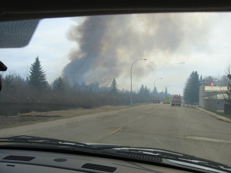Fire trucks on road with smoke plume in background