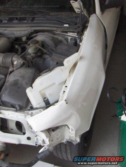 2003 Ford Crown Victoria - The front fender of a white vehicle is severely damaged, revealing the engine components underneath.