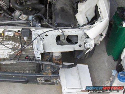 2003 Ford Crown Victoria - The front end of a white 2003 Ford Crown Victoria shows significant damage, with the grille and surrounding components exposed.