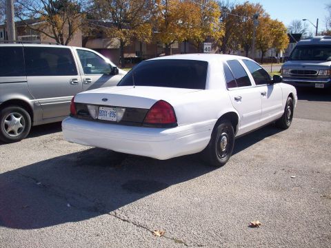 2003 Ford Crown Victoria - A white 2003 Ford Crown Victoria sedan is parked next to a silver minivan and a dark van.