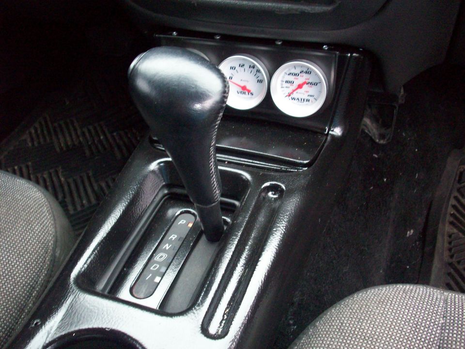 car's center console with gear shifter and two aftermarket gauges for volts and water temp