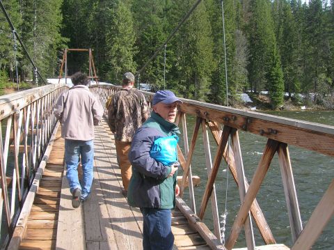 1996 Ford Bronco - People cross a wooden suspension bridge in a wooded area with a river below.