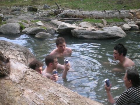 1996 Ford Bronco - Friends enjoy a soak in a natural hot spring, holding cans of soda amidst rocks and fallen logs.