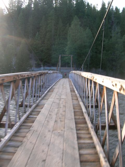 1996 Ford Bronco - A person walks across a wooden suspension bridge spanning a river, surrounded by dense forest.