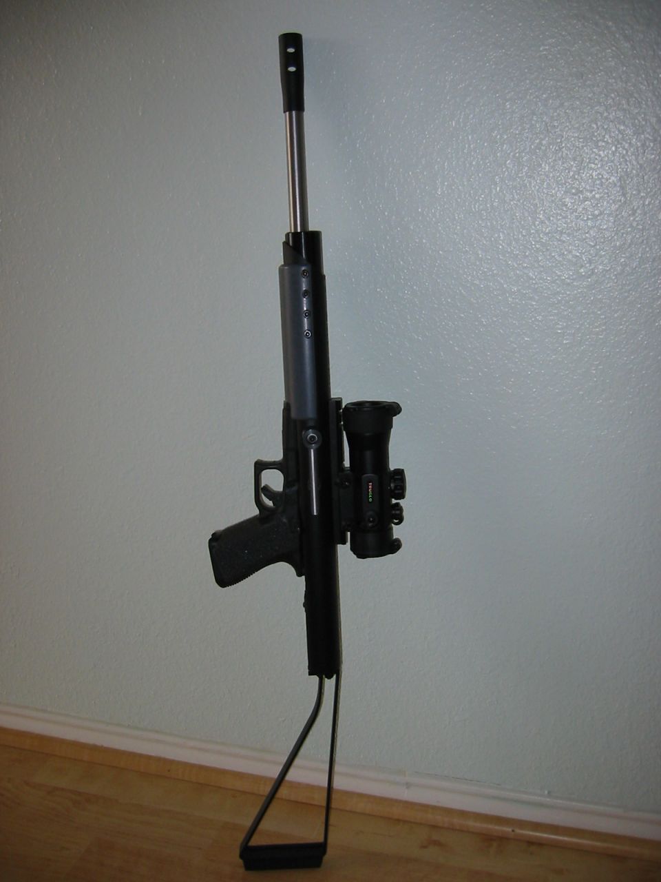 Rifle with scope and bipod, leaning against a wall