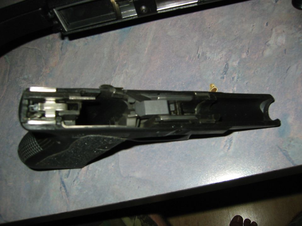 Black gun frame with internal mechanisms visible, resting on a textured surface