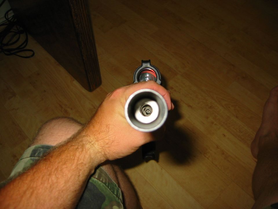 Hand holding a metal tube with internal spring mechanism. Wood floor and furniture visible