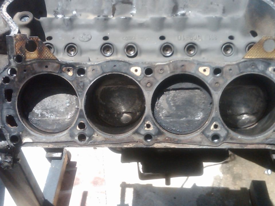 Bare V8 engine block deck with carbon-caked piston tops