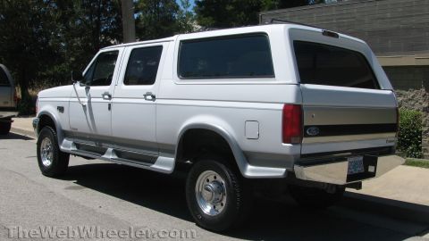 1996 Ford C-350 (Centurion Conversions) - This white SUV with a camper shell is seen from the rear quarter angle.