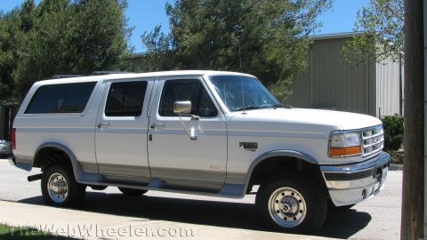 1996 Ford C-350 (Centurion Conversions) - A white extended SUV is parked on the side of the road in front of a building.