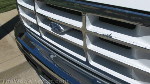 1996 Ford C-350 (Centurion Conversions) - Close-up of a white Ford truck's front grille and chrome bumper, revealing the Ford emblem and signs of wear.