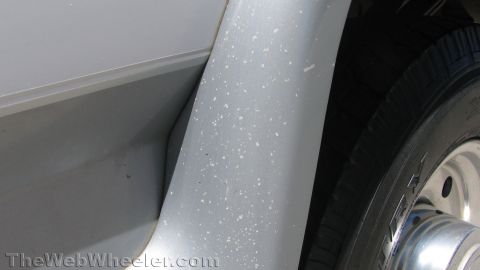 1996 Ford C-350 (Centurion Conversions) - Tight close-up of the gray lower rocker panel and wheel-arch flare on a white truck, the flare speckled with white paint or road-debris spa…