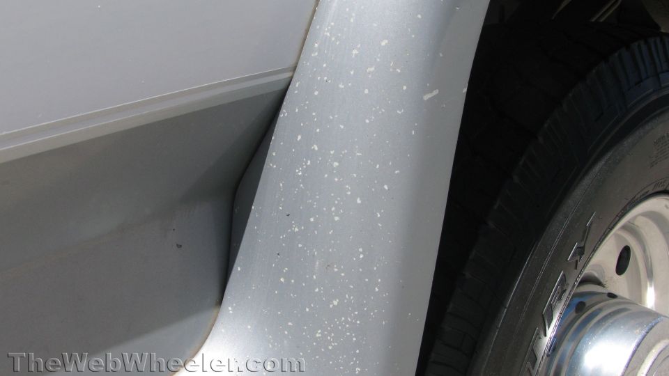 Close-up of gray rocker panel and wheel flare with paint speckles beside a chrome wheel