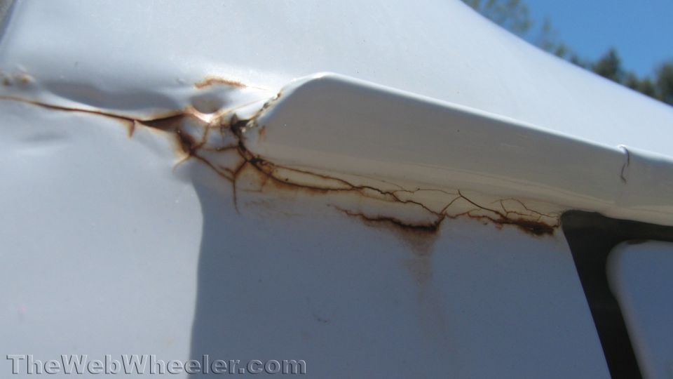 White vehicle body showing rust and cracked paint near a seam