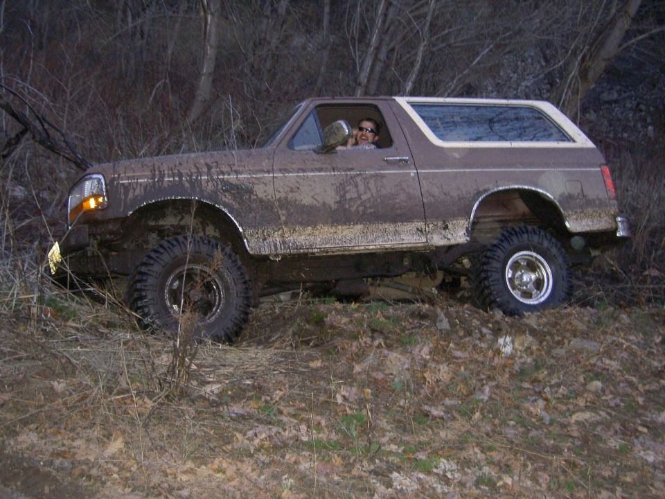Mud-covered 1992 Ford Bronco driving through brush, driver visible