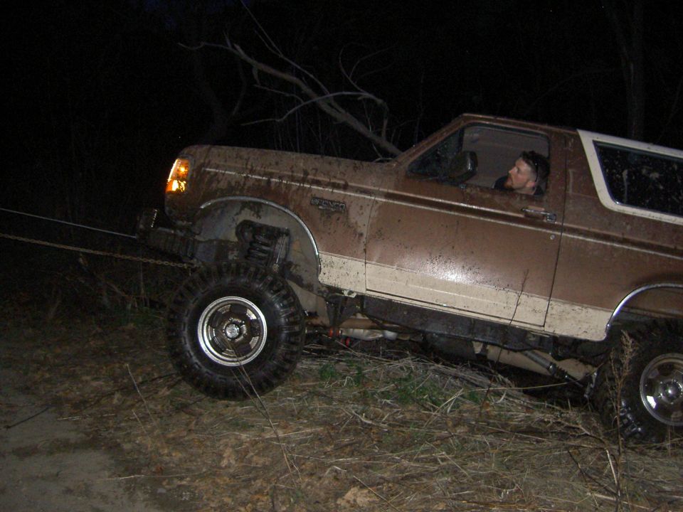 Brown and white 1992 Ford Bronco stuck in mud, driver visible