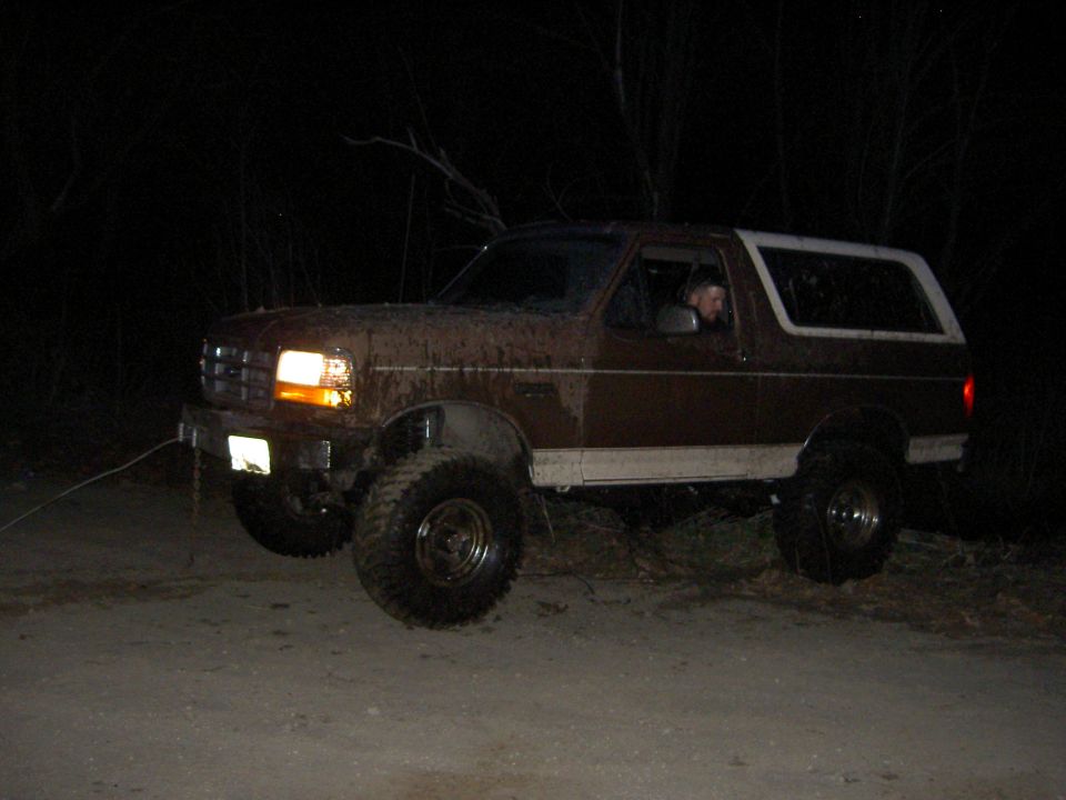 Muddy 1992 Ford Bronco with lifted suspension and large tires on a dirt road at night