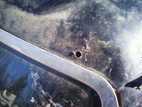 1990 Ford Bronco - Close-up of a black vehicle hood showing two circular rust holes and a piece of chrome trim.