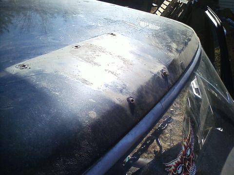 1990 Ford Bronco - The weathered hood and windshield of a vehicle are shown, with visible rust and a chain in the foreground.
